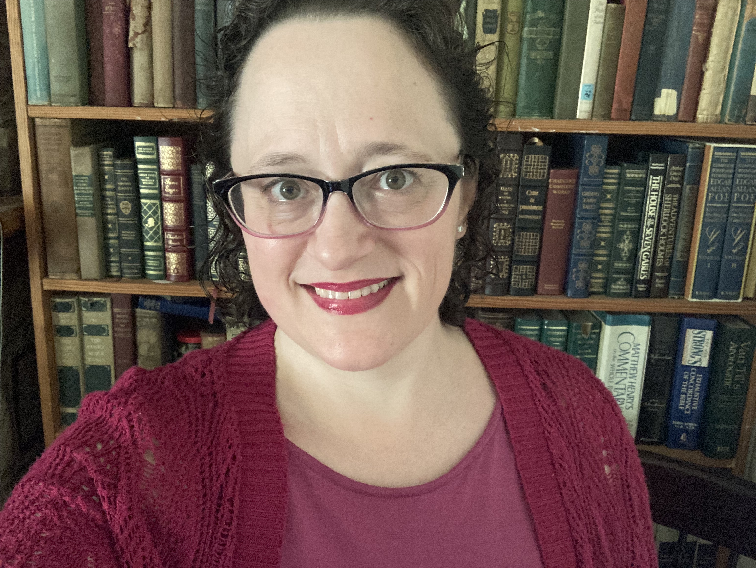 selfie of woman with dark brown hair and glasses in a pink dress and crocheted sweater